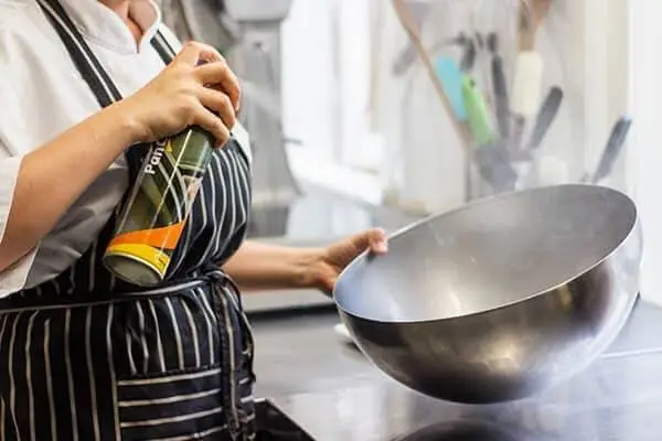 Restaurant cook spraying a metal bowl with oil.