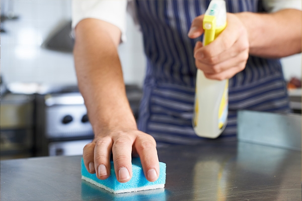man cleaning kitchen with soap bottle and sponge on countertop.