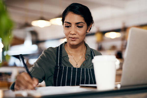 woman taking notes on notepad next to laptop