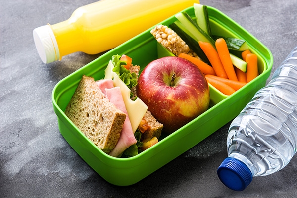 Sandwich, apple, and sliced veggies in a school bento box lunch container.