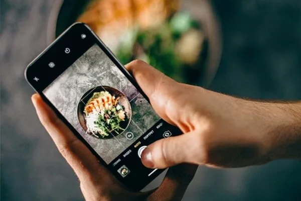 person holding phone and taking a photo of food dish on plate