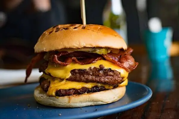 Double patty cheeseburger with bacon on a plate and a wooden toothpick in the middle.