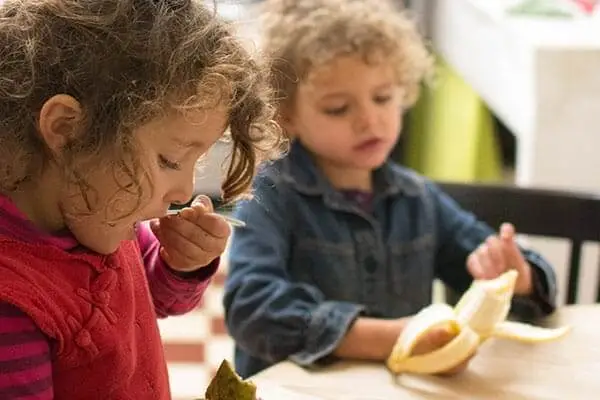 Two kids eating a banana at a table.