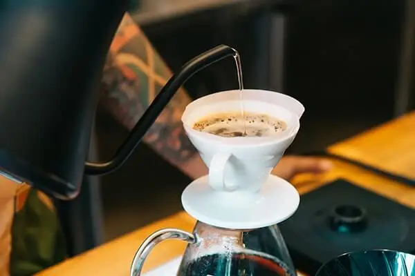 Tattooed coffee shop barista brewing a cup of pour over espresso