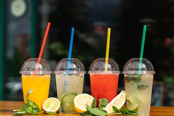 Four margaritas in to-go cups on top of a countertop with limes.