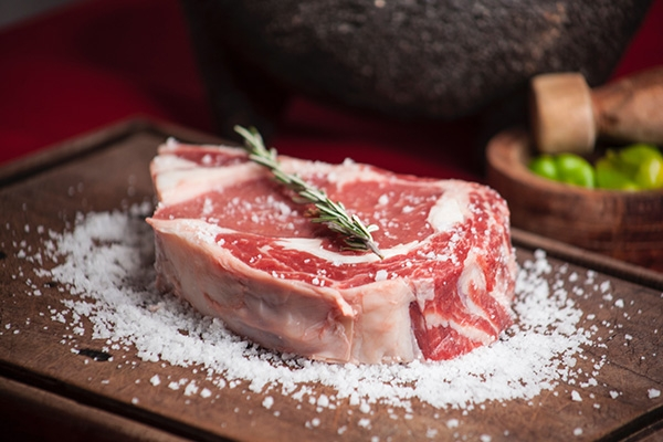 Steak on a bed of salt with a sprig of rosemary on top.