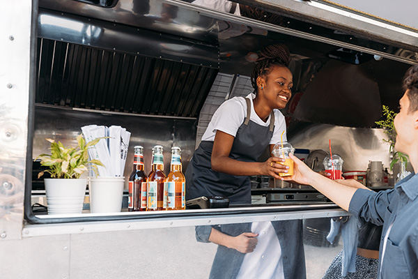 woman in food truck passes drink to customer.