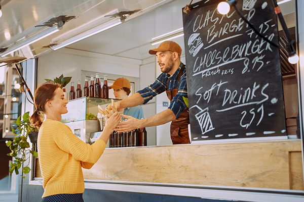man handing a woman her order from a food truck menu