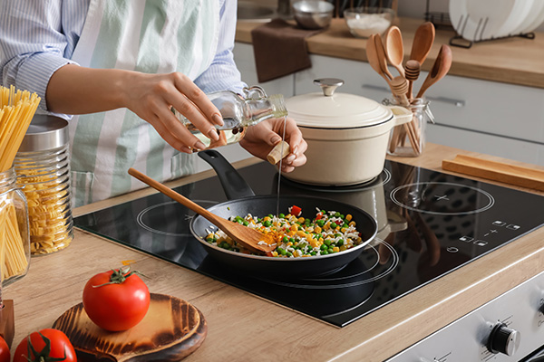 woman pouring cooking oil into pan with sauteed vegetables