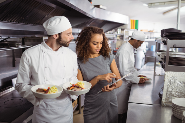 Chefs in restaurant kitchen looking at clipboard with manager