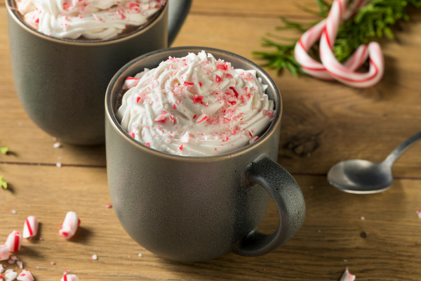 Two hot drinks in mugs with whipped cream and peppermint on top