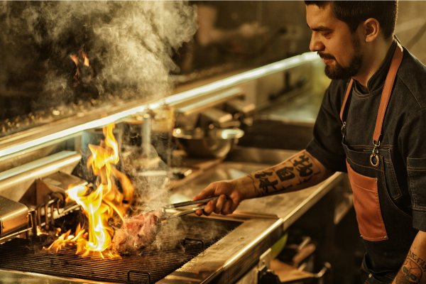 Restaurant cook grills meet on flaming grill
