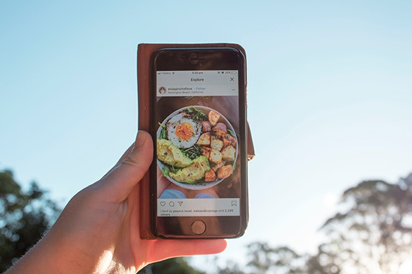 Person holding up a smartphone showing an Instagram picture of a salad.