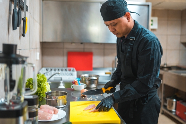 Chef slicing raw chicken on a yellow cutting board.