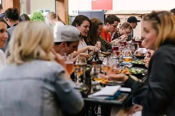 Group of people at a restaurant with tables full of food and drinks.