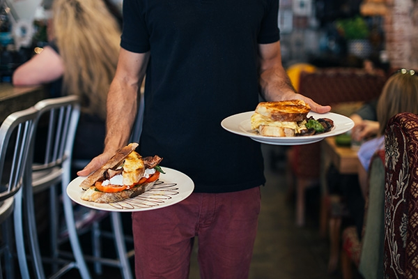Restaurant server in a black shirt carrying a sandwich plate in each hand.