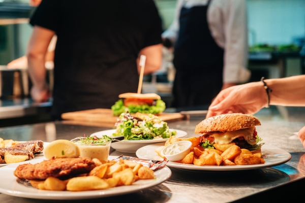 Burgers, fries, and salad on a restaurant table with chefs preparing food in the background.