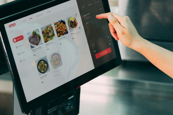 Restaurant employee using a POS touchscreen showing menu items.