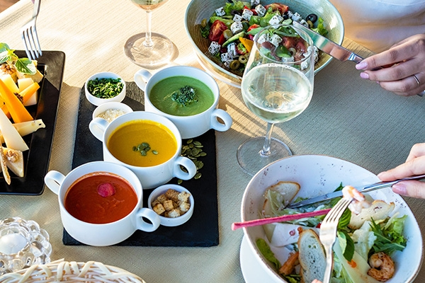 Table with two salads, wine glasses, and various sauces.