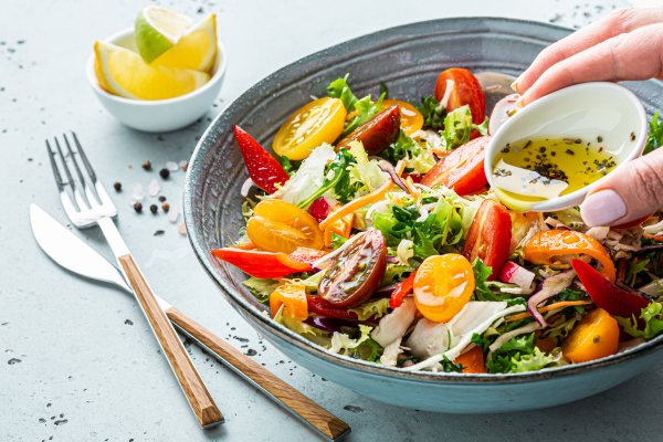 Fresh bright-colored salad in bowl on table with hand pouring vinaigrette dressing on it