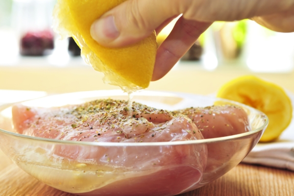 squeezing lemon on raw marinating chicken.