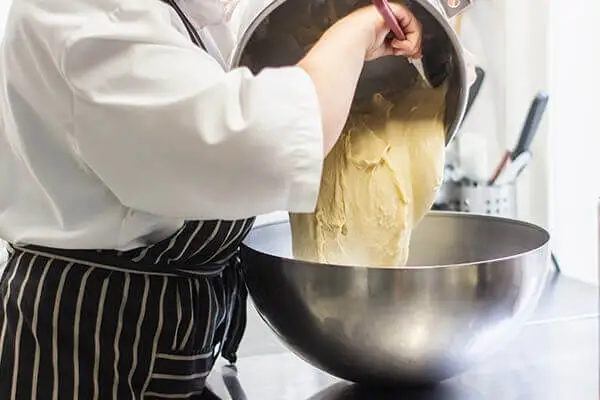 Baker transferring dough from a mixer to a bowl.