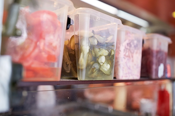 Diced tomatoes, cucumbers, and red onions in storage containers in a refrigerator.