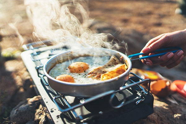 Person cooking fired eggs on a campfire gas burner.