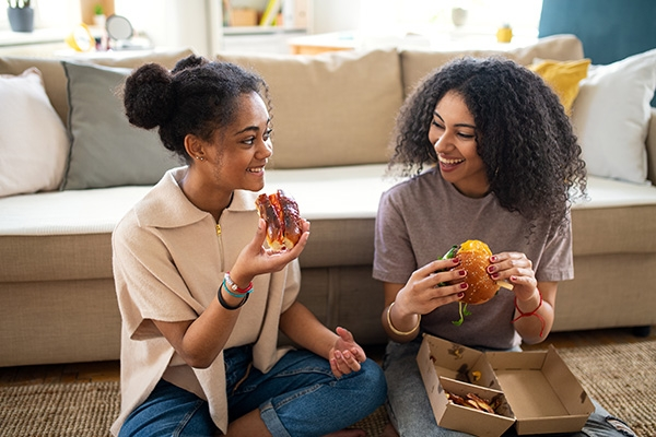 Two women sitting on the floor in front of a couch eating takeout.
