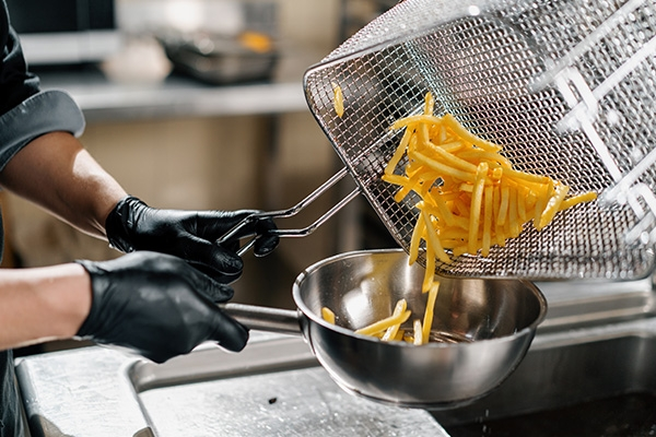 Chef moving fries from a fryer to a stainless steel bowl.
