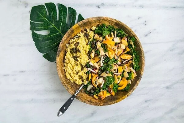 Wooden bowl of a vegan salad with a spoon sticking out of the food.
