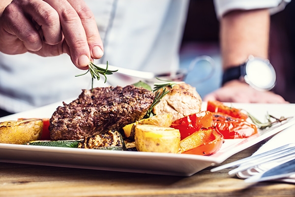 Chef placing rosemary on top of a steak dish.