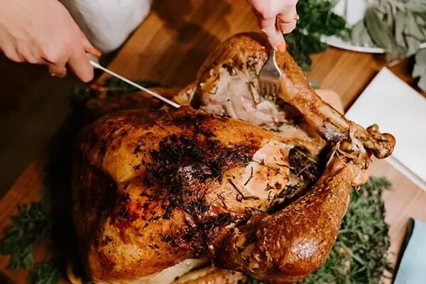 Person carving a turkey on a wooden cutting board.