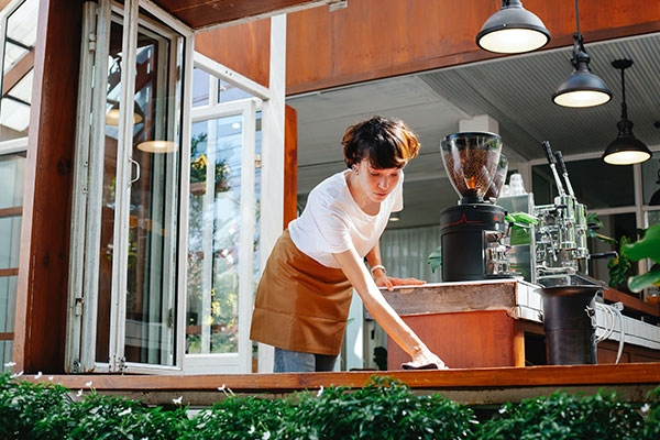 Woman wiping down a wooden table outside of a restaurant.